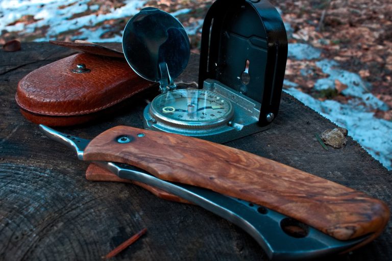 pocket knife and compass on wooden log